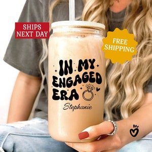 May include: A clear glass tumbler with a black and white graphic that says "In My Engaged Era" with a diamond ring illustration and the name "Stephanie".