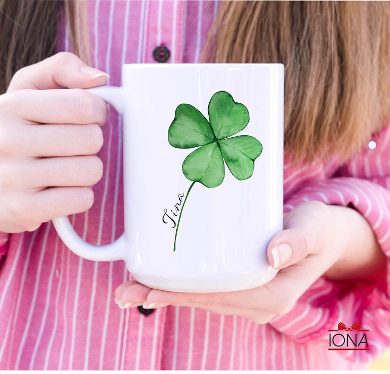 May include: White ceramic mug with a green four-leaf clover design and the name "Tina" written in cursive.