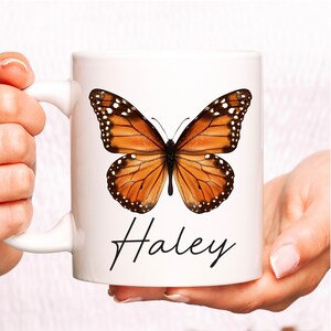 May include: White ceramic coffee mug with a brown and black monarch butterfly graphic and the name "Haley" written in black cursive.