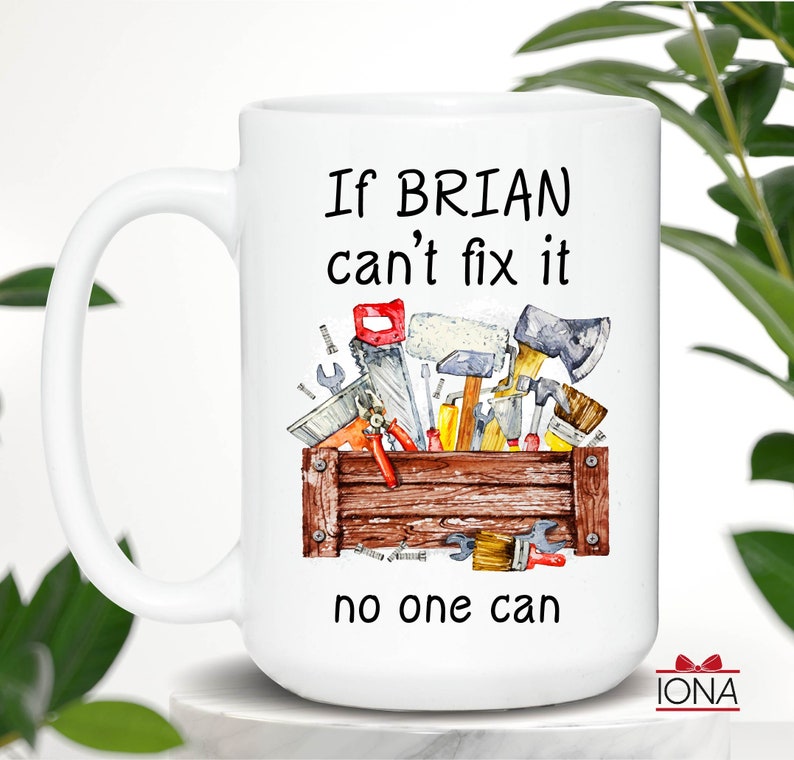 May include: White ceramic mug with a handle, featuring a watercolor illustration of a wooden toolbox filled with tools. The mug has the text "If BRIAN can't fix it no one can" in black.