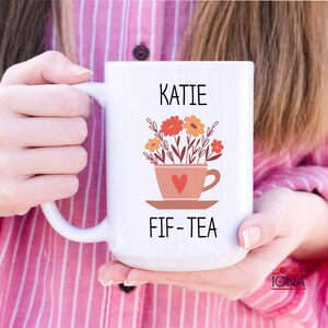 May include: White ceramic mug with a floral design and the text "KATIE FIF-TEA".