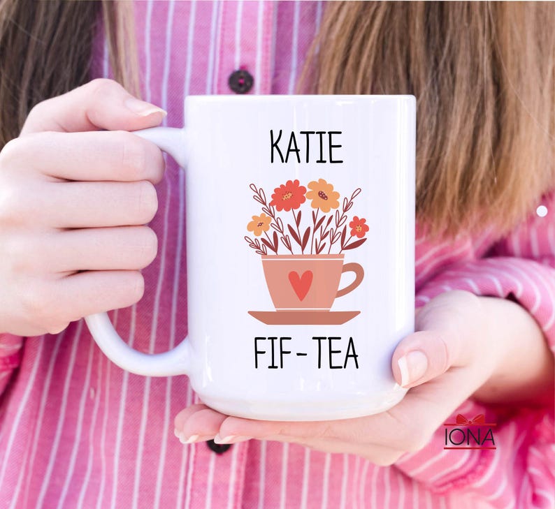 May include: White ceramic mug with a floral design and the text "KATIE FIF-TEA".