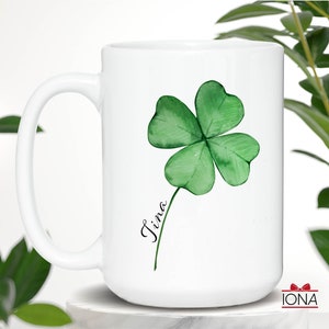 May include: White ceramic mug with a green four-leaf clover design and the name "Tina" written in black cursive.