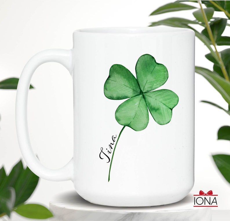 May include: White ceramic mug with a green four-leaf clover design and the name "Tina" written in black cursive.