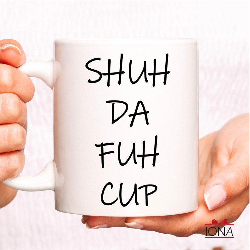 K&ouml;nnte beinhalten: Wei&szlig;e Keramiktasse mit schwarzem handgeschriebenem Text, der "SHUH DA FUH CUP" lautet.