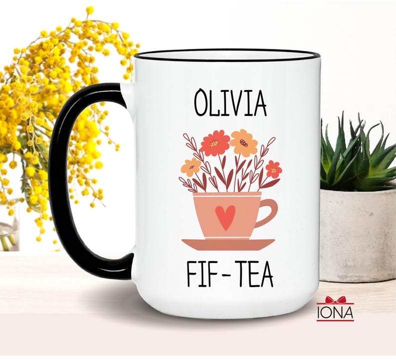 May include: White ceramic mug with a black rim and handle. The mug has a floral design with a teacup and the text "Olivia Fif-Tea".