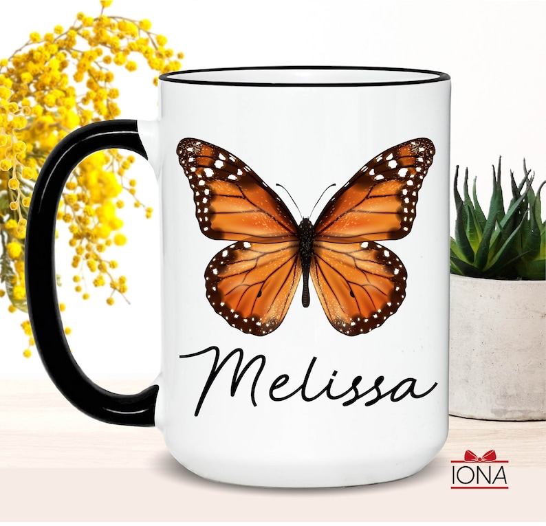May include: White ceramic coffee mug with a black handle and a black rim. The mug features a colorful butterfly illustration and the name "Melissa" in black cursive writing.