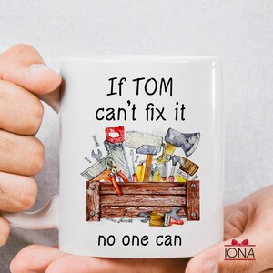 May include: White ceramic mug with the text "If TOM can't fix it, no one can." The mug features a watercolor illustration of a wooden toolbox filled with various tools, including a saw, hammer, and wrench.