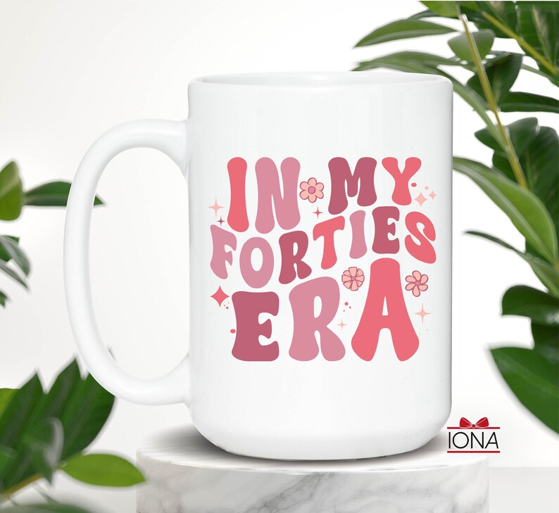 May include: White ceramic mug with the text "IN MY FORTIES ERA" in shades of pink and red. The mug has a large handle and is decorated with flowers and stars. The mug is a perfect gift for someone celebrating their 40th birthday.