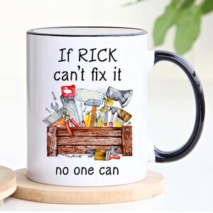 May include: White ceramic mug with a black handle and rim. The mug features a watercolor illustration of a toolbox filled with tools. Text on the mug reads "If RICK can't fix it, no one can."