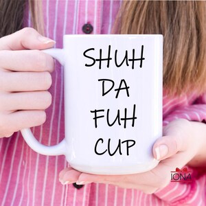 K&ouml;nnte beinhalten: Wei&szlig;e Keramiktasse mit schwarzem Text, der "SHUH DA FUH CUP" lautet.