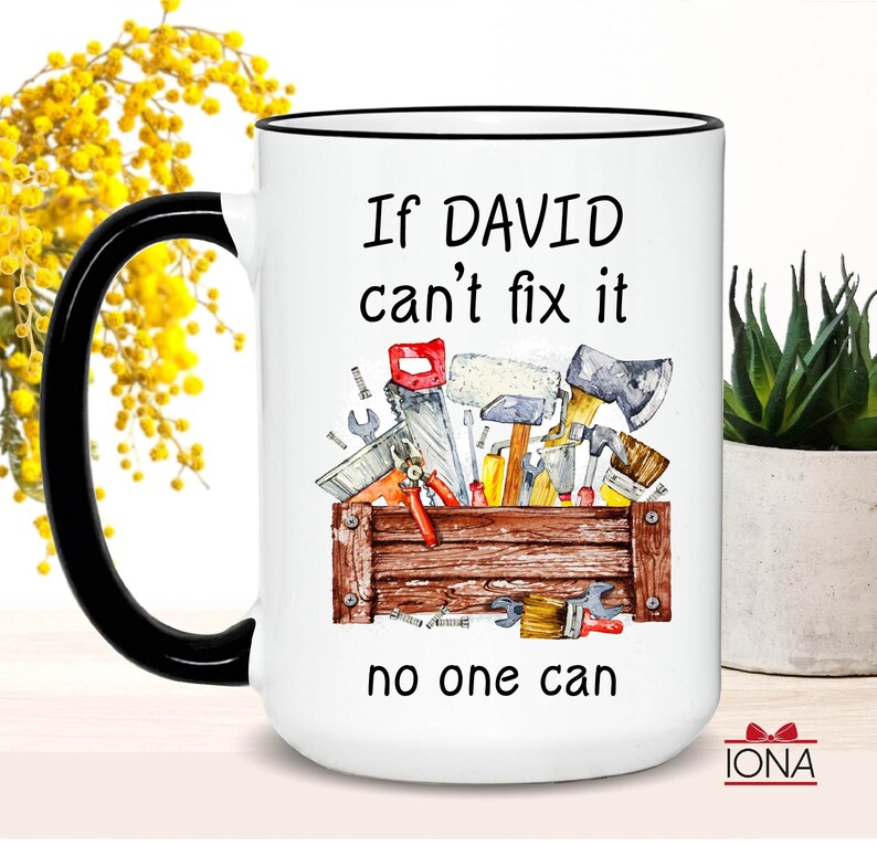 May include: White ceramic mug with a black handle and rim. The mug features the text "If DAVID can't fix it no one can" and a watercolor illustration of tools in a wooden toolbox. The mug is a gift for a handyman.