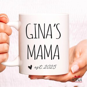 Puede incluir: Taza de cer&aacute;mica blanca con texto negro que dice "GINA'S MAMA est. 2025" con un peque&ntilde;o coraz&oacute;n negro.