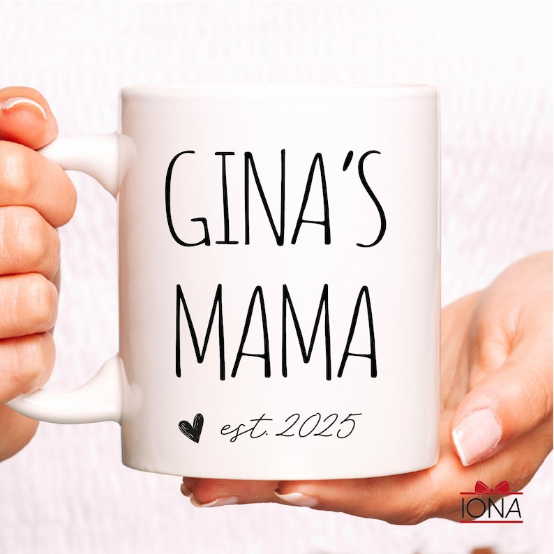 Puede incluir: Taza de cer&aacute;mica blanca con texto negro que dice "GINA'S MAMA est. 2025" con un peque&ntilde;o coraz&oacute;n negro.