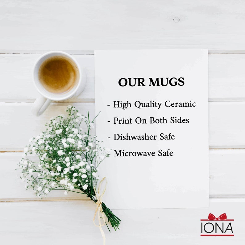 May include: White ceramic mug with the text "OUR MUGS" and a list of features: High Quality Ceramic, Print On Both Sides, Dishwasher Safe, Microwave Safe. The mug is sitting on a white wooden surface with a bouquet of white flowers.