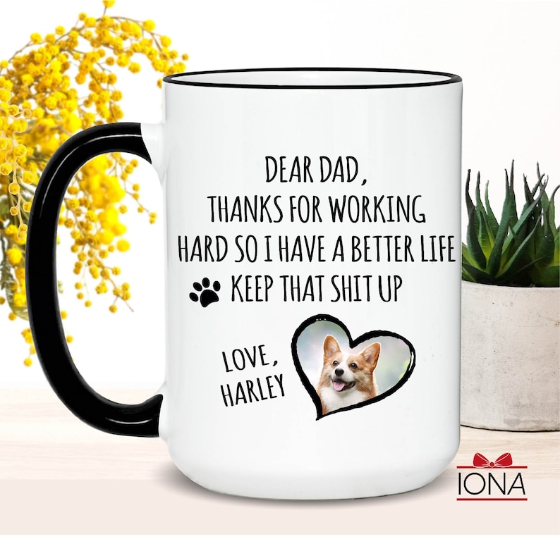 May include: White ceramic coffee mug with a black handle and rim. The mug features a black paw print, a heart with a photo of a corgi, and the text "Dear Dad, Thanks for working hard so I have a better life. Keep that shit up. Love, Harley."