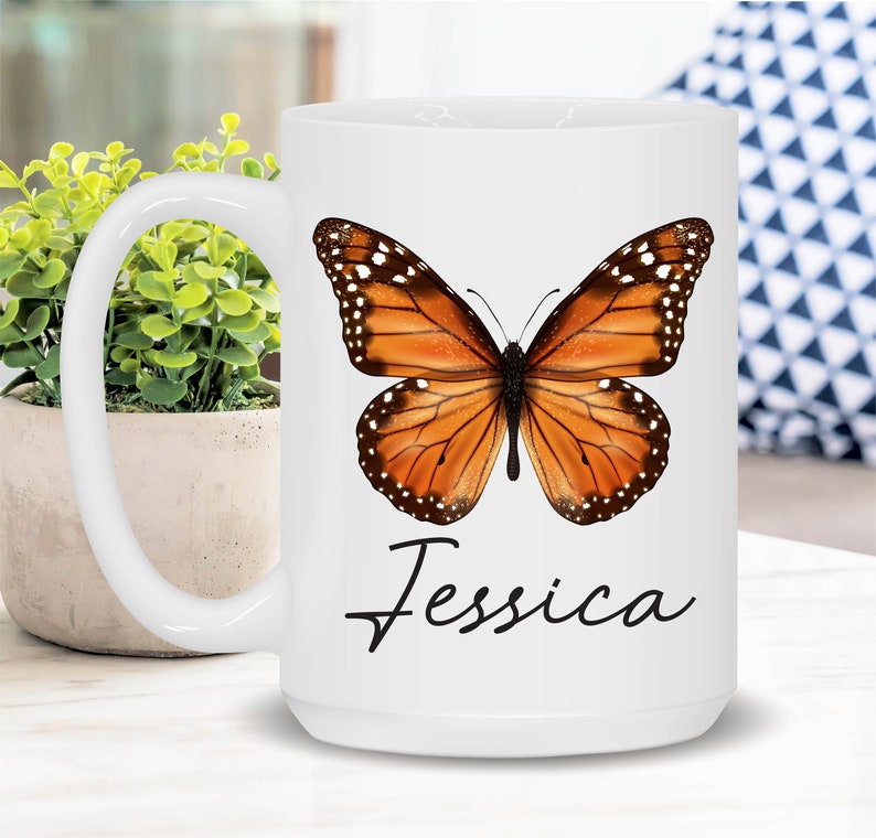 May include: White ceramic mug with a butterfly design and the name "Jessica" printed on the front. The butterfly is orange and black with white spots.
