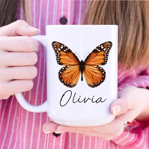 May include: White ceramic mug with a brown and orange butterfly graphic and the name "Olivia" written in black cursive.
