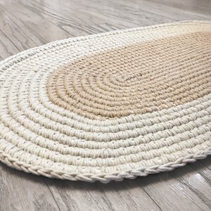 May include: A hand-woven oval rug with a beige and white color gradient. The rug is made of thick, natural fibers and has a textured surface.