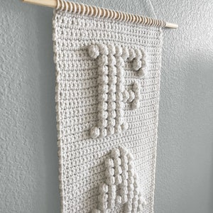 May include: A white crocheted wall hanging with the word "Peace" spelled out in raised stitches.
