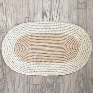 May include: A white and beige oval-shaped crocheted rug with a textured design.