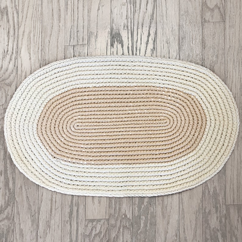 May include: A white and beige oval-shaped crocheted rug with a textured design.