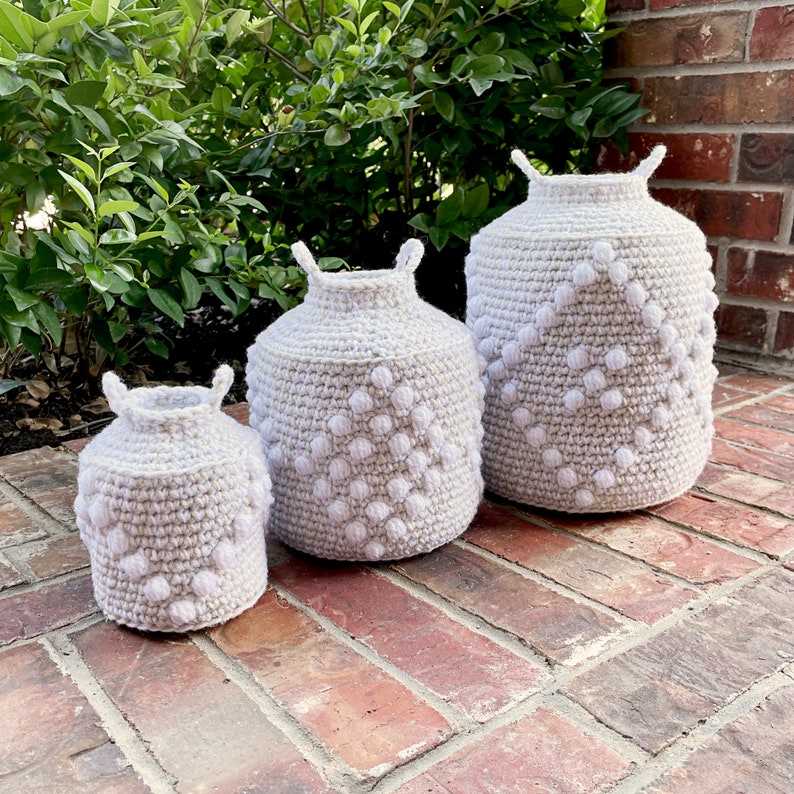 May include: Three crocheted baskets in various sizes, all with a white and gray color scheme. The baskets have a textured design with raised white circles.