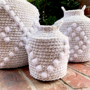 May include: Three crocheted baskets with a white and beige pattern. The baskets are made with a textured stitch and have a round shape.