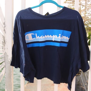May include: A navy blue cropped t-shirt with a white "Champion" logo and blue and white stripes.