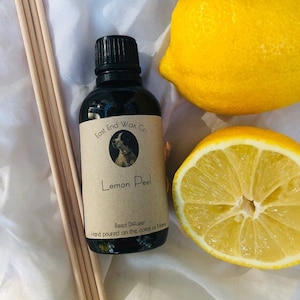 May include: A black glass bottle of "Lemon Peel" reed diffuser with a black cap, a label with a dog illustration, and wooden reeds. Two yellow lemons, one whole and one halved, are next to the bottle. The text "East End Wax Co." is visible.