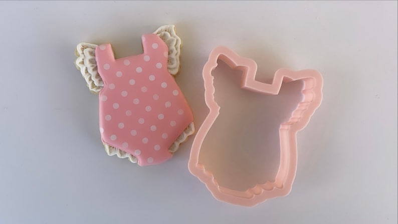 Peut inclure: Emporte-pi&egrave;ce en forme de barboteuse pour b&eacute;b&eacute; avec un motif de pois rose et blanc et une bordure festonn&eacute;e.