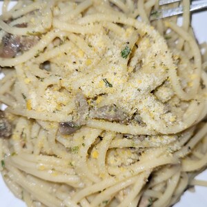May include: A close-up of a plate of spaghetti with mushrooms and a white sauce, topped with grated cheese.