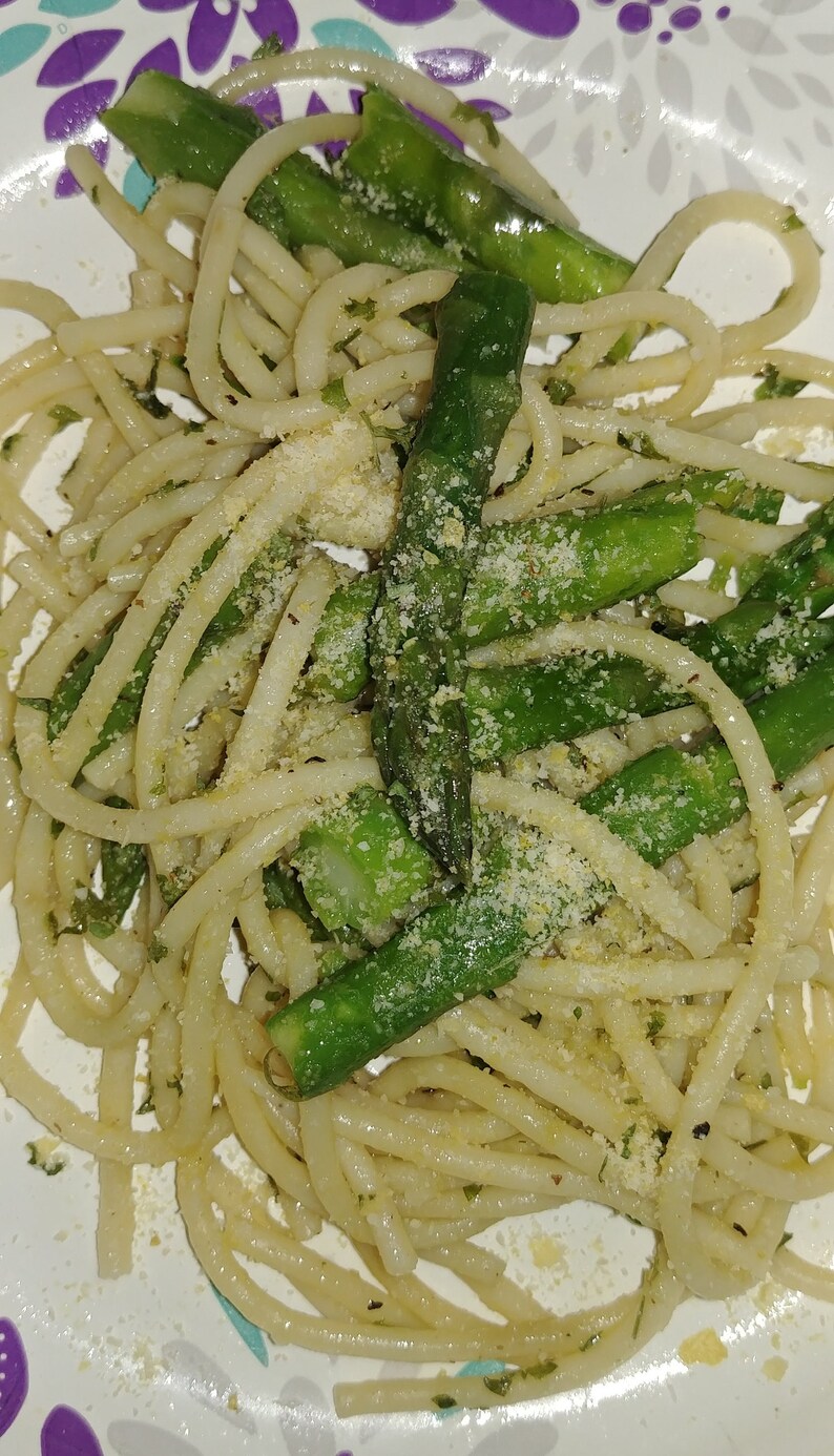 May include: A plate of spaghetti with asparagus and parmesan cheese. The spaghetti is cooked al dente and the asparagus is tender-crisp. The parmesan cheese is grated and sprinkled over the top.