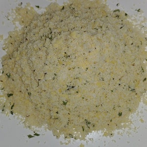 May include: A close-up of a pile of light yellow breadcrumbs with green herbs mixed in.