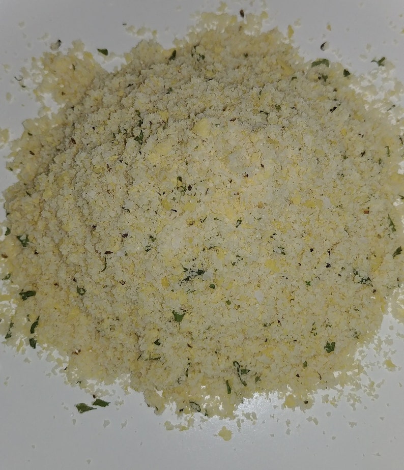 May include: A close-up of a pile of light yellow breadcrumbs with green herbs mixed in.
