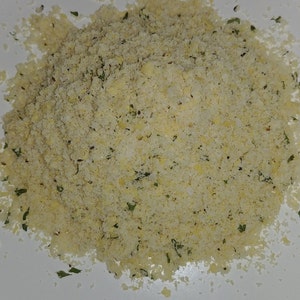 May include: A close-up of a pile of light yellow breadcrumbs with green herbs mixed in.