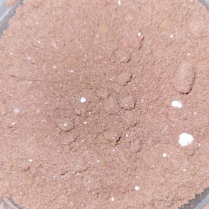 May include: A close-up of a brown powder with white specks in a clear container.