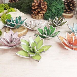 May include: Assortment of stained glass succulent decorations in various colors, including pink, green, white, and orange. The succulents are arranged on a light wood surface.