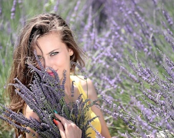 May include: A woman holding a bouquet of lavender flowers in a field of lavender. She is wearing a yellow top and has long brown hair. The lavender flowers are purple and green.