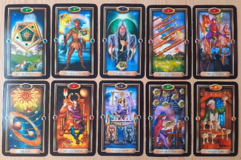 May include: A collection of tarot cards with black borders and gold accents. Each card features detailed illustrations and titles such as "Ace of Pentacles," "The Magician," and "The Sun." The cards are arranged in rows, showcasing various scenes and figures.