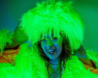 May include: A person wearing a bright green fluffy hat and jacket. The hat and jacket are made of faux fur. The person is smiling and has a nose ring.