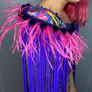 Puede incluir: Un ribete de plumas y flecos de color morado y rosa con una base de tela de estampado floral colorido. El ribete es perfecto para a&ntilde;adir un toque de fantas&iacute;a a cualquier prenda o accesorio.