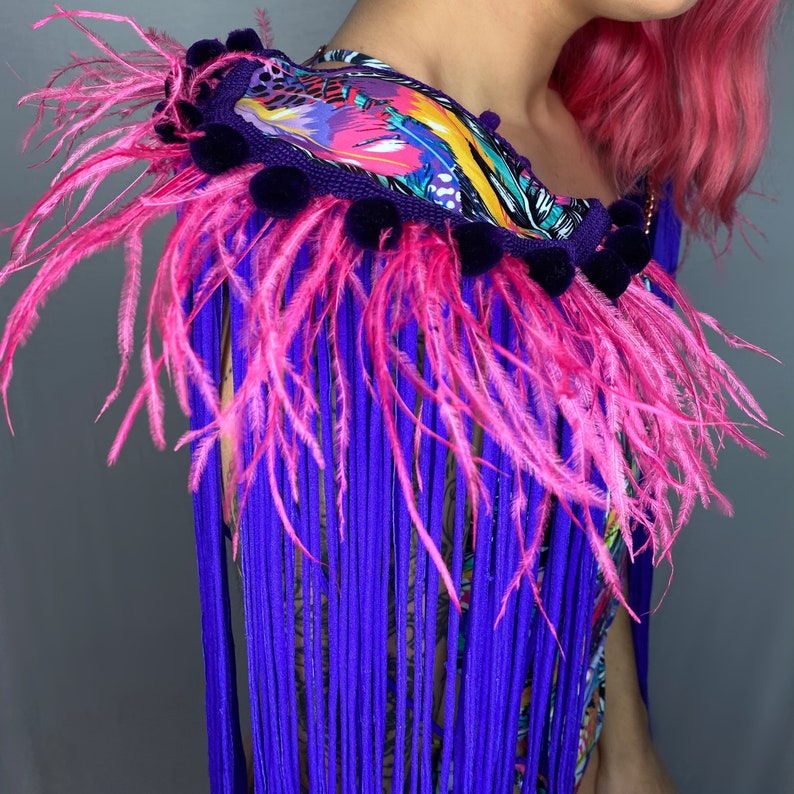 Puede incluir: Un ribete de plumas y flecos de color morado y rosa con una base de tela de estampado floral colorido. El ribete es perfecto para a&ntilde;adir un toque de fantas&iacute;a a cualquier prenda o accesorio.