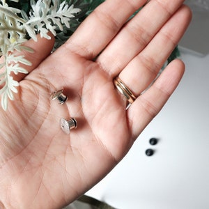 以下が含まれることがあります： 手の中に、2つの銀色の金属製スナップファスナー（ポッパーまたはプレススタッドとも呼ばれます）があります。ファスナーは、衣服やその他の布地プロジェクトによく使用されます。