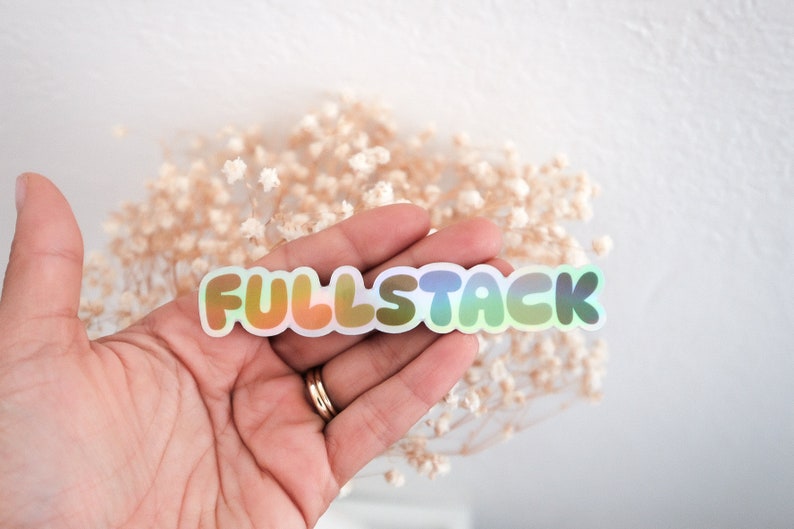 K&ouml;nnte beinhalten: Ein holografischer Aufkleber mit dem Text "FULLSTACK" in einem Regenbogen-Farbschema. Der Aufkleber wird in einer Hand gehalten.