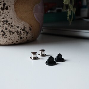 以下が含まれることがあります： 銀色の金属製のピンバック留め具2つと黒いプラスチック製のピンバック留め具2つ