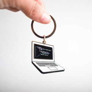 Peut inclure: Un porte-cl&eacute;s argent&eacute; avec un charme en forme d'ordinateur portable. L'ordinateur portable a un &eacute;cran noir avec du code color&eacute; dessus.