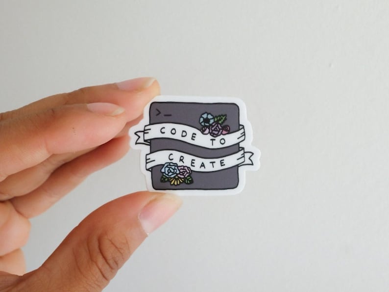 Op de afbeelding: Een grijze sticker met een codesymbool, bloemen en de tekst "Code to Create" op een witte banner.