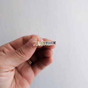 May include: A gold-colored pin with the word "FULLSTACK" spelled out in rainbow colors. Each letter is outlined in gold.