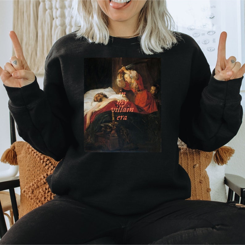 A black book lover sweatshirt featuring a painting of a woman and a sword with the text 'in my villain era'. The perfect bookish gift.